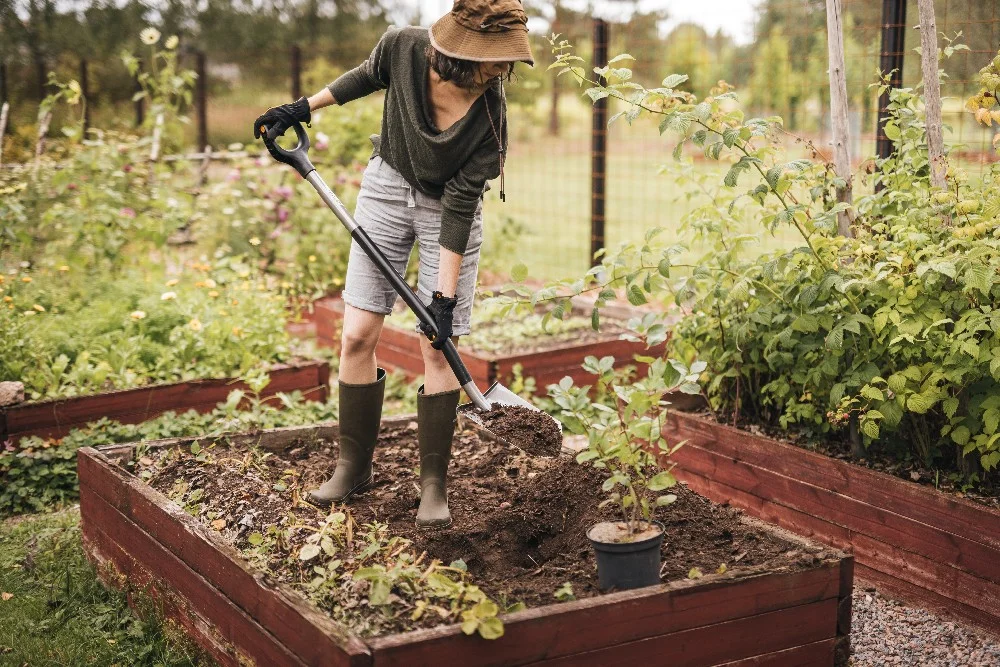 Person pflanzt mit einem Spaten etwas in ein Hochbeet ein.